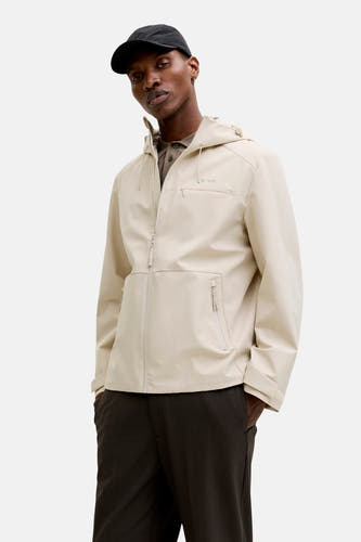 Ecrukleurige korte jas van PREMIUM by JACK & JONES, met capuchon en zakken met ritssluiting, gedragen met een pet en pantalon.
