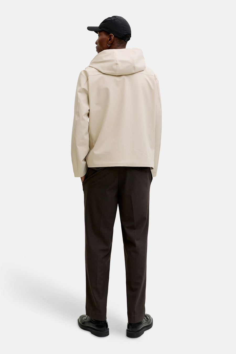 Ecru korte jas van PREMIUM by JACK & JONES, met capuchon, gecombineerd met donkere pantalon en zwarte schoenen, gezien vanaf de achterkant.