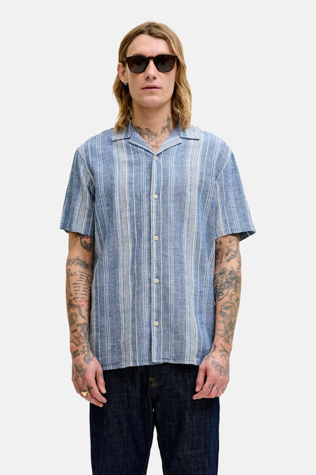 Chemise bleue à rayures à manches courtes de PREMIUM BLUE by JACK & JONES, avec des tatouages sur les bras et des lunettes de soleil.