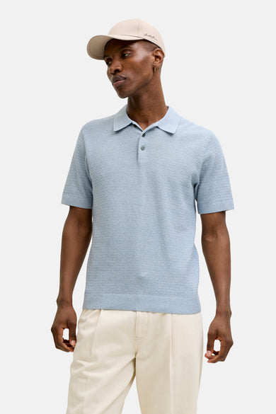 Blauw poloshirt met korte mouwen van PREMIUM BLUE by JACK & JONES, met een fijne textuur en gedragen met een beige broek en pet.
