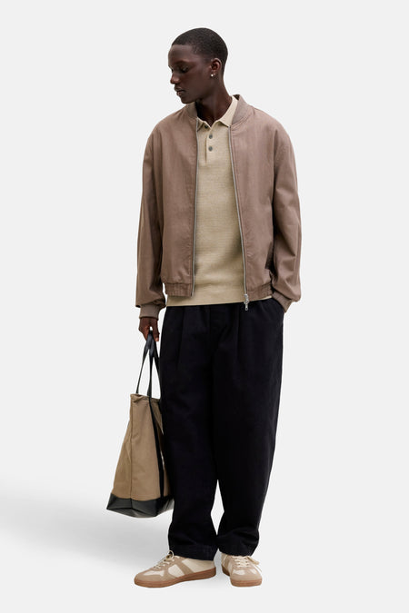 Beige polo met korte mouwen van PREMIUM BLUE by JACK & JONES, gedragen onder een bruin bomberjack, met zwarte broek en beige schoenen.