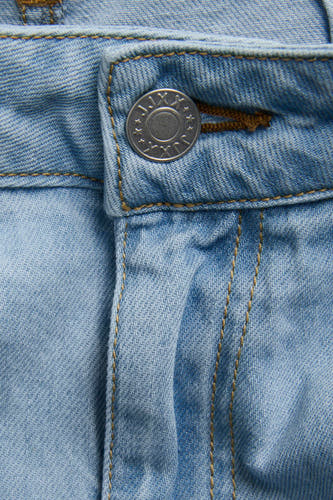 Lichtblauwe denim wijde jeans van JJXX, met een zilveren knoop en bruine stiksels in close-up.
