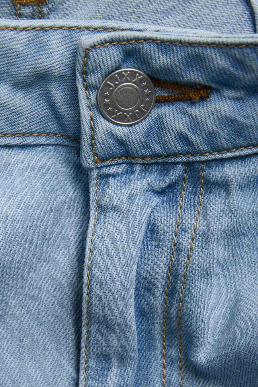 Lichtblauwe denim wijde jeans van JJXX, met een zilveren knoop en bruine stiksels in close-up.
