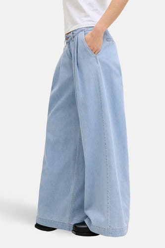 Lichtblauwe wijde jeans van JJXX, met een hand in de zak, gecombineerd met een wit shirt en zwarte schoenen.
