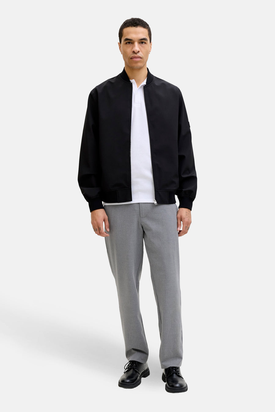Grijze broek van JACK & JONES JEANS INTELLIGENCE, gecombineerd met een wit poloshirt en een zwart bomberjack.