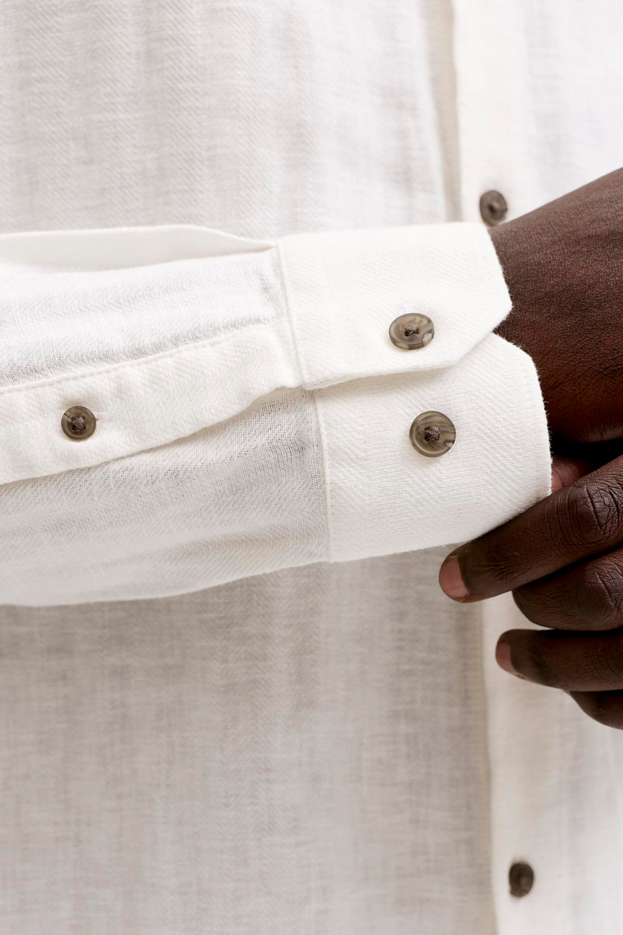 Wit overhemd van PREMIUM by JACK & JONES met herringbone-textuur, knoopmanchetten en een hand die de mouw vasthoudt.