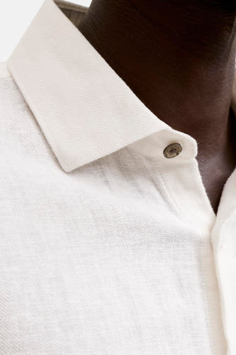 Wit hemd van PREMIUM by JACK & JONES met een geweven textuur, fijne visgraat op de kraag en donkere knoop, gedragen bij een donkere huidskleur.
