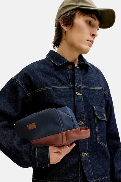 Blauwe toilettas van ACCESSORIES BY JACK & JONES met bruine lederen accenten, gedragen door een model in denim jack en pet.
