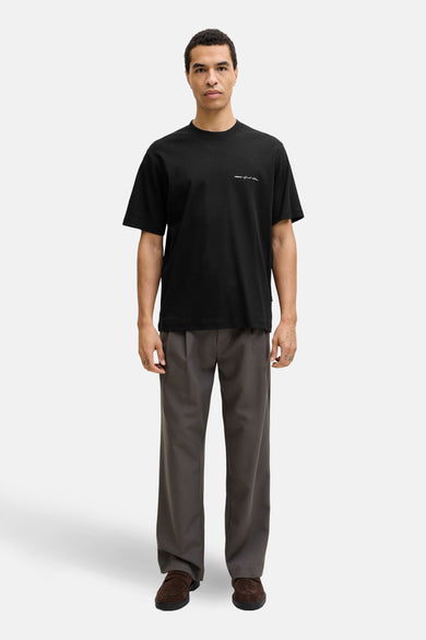 T-shirt noir à manches courtes de PREMIUM by JACK & JONES, avec un imprimé texte discret, porté avec un pantalon gris et des mocassins en daim.