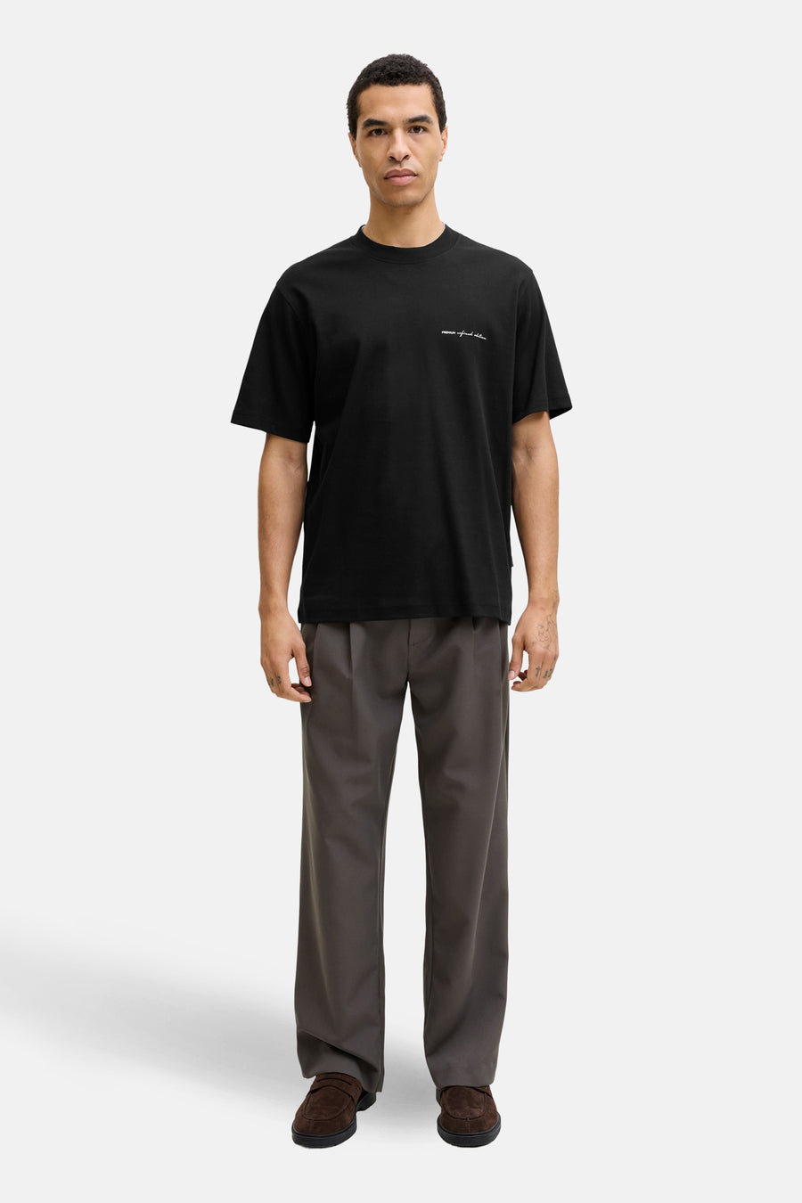 T-shirt noir à manches courtes de PREMIUM by JACK & JONES, avec un imprimé texte discret, porté avec un pantalon gris et des mocassins en daim.