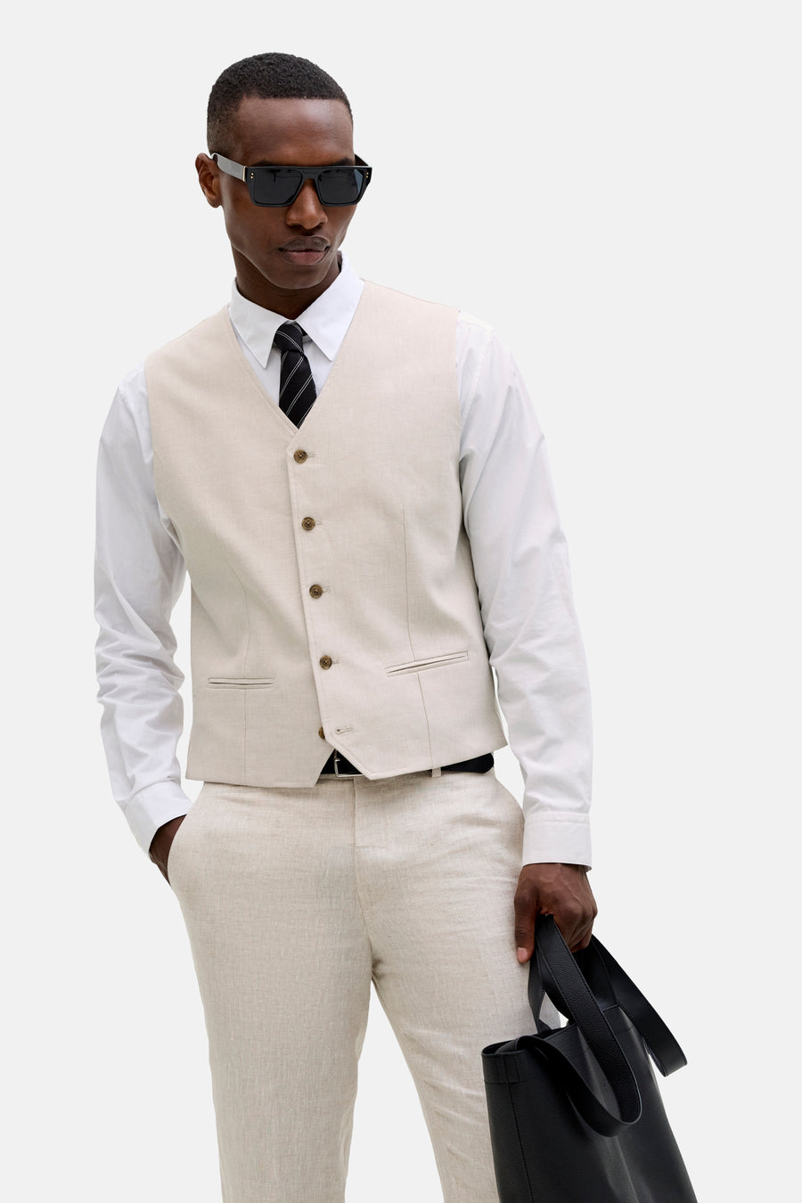 Ecru gilet van PREMIUM by JACK & JONES, gedragen over een wit overhemd met een gestreepte stropdas en een zwarte tas.