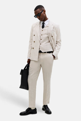 Ecru gilet van PREMIUM by JACK & JONES, gedragen over een wit overhemd met gestreepte das, onder een beige pak met tas.
