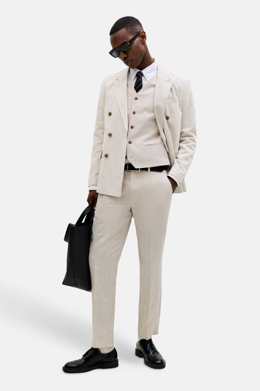 Ecru gilet van PREMIUM by JACK & JONES, gedragen over een wit overhemd met gestreepte das, onder een beige pak met tas.
