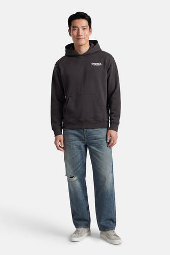 Grijze sweater met kap van CORE BY JACK & JONES, met zak op de buik, gecombineerd met blauwe jeans en grijze sneakers.
