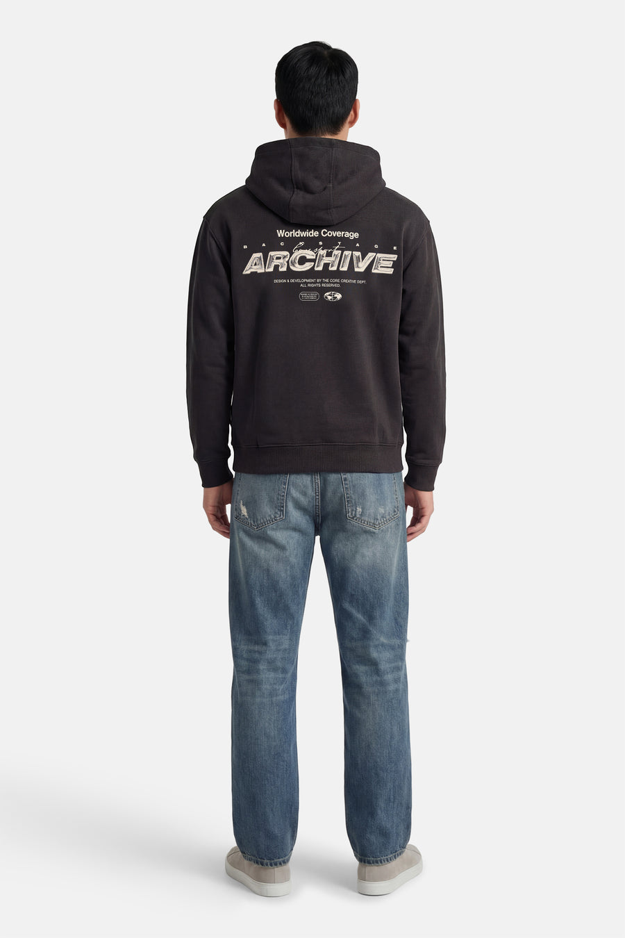 Grijze sweater met kap van CORE BY JACK & JONES, met print op de rug, gecombineerd met blauwe jeans en grijze schoenen.