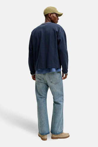 Blauwe sweater van ORIGINALS BY JACK & JONES, met een subtiel gestreept patroon, gecombineerd met jeans en een kaki pet.
