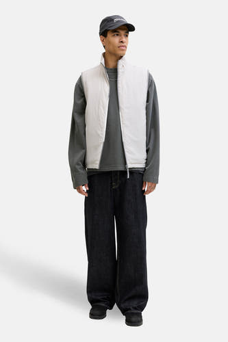 Zwarte sweater met ronde hals van CORE BY JACK & JONES, gecombineerd met een witte bodywarmer, wijde jeans en een pet.