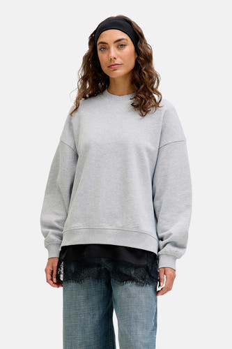 Grijze sweater van JJXX, met lange mouwen, gedragen over een zwarte top met kanten rand, en blauwe jeans.
