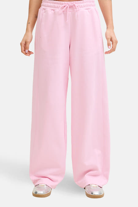 Pantalon de jogging rose de JJXX, à jambes larges et avec un cordon de serrage à la taille, porté avec un t-shirt blanc et des chaussures argentées.