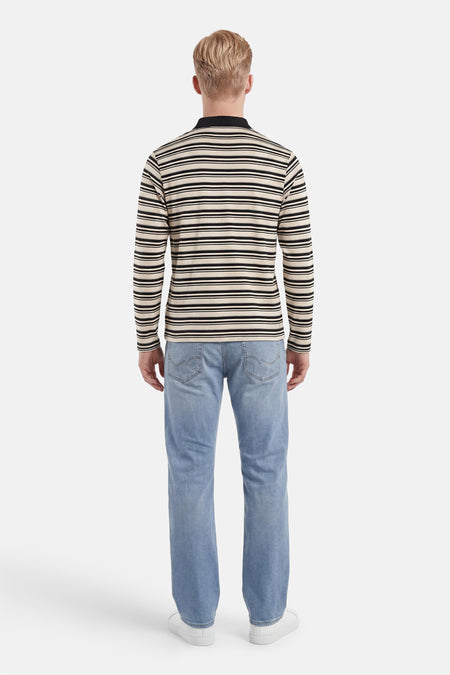 Multicolor polo met lange mouwen van ORIGINALS BY JACK & JONES, met crème- en zwarte horizontale strepen en zwarte polokraag, van achteren gezien op een man in jeans en witte sneakers.