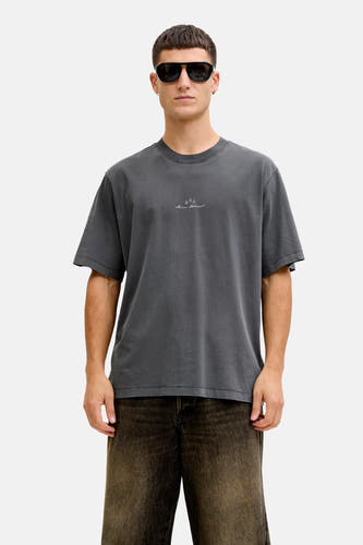 T-shirt noir à manches courtes de CORE BY JACK & JONES, avec un petit logo sur la poitrine, porté avec un pantalon marron et des lunettes de soleil.