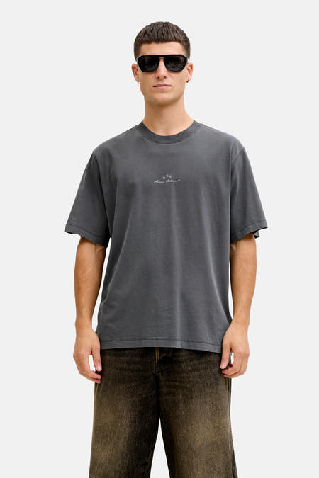 T-shirt noir à manches courtes de CORE BY JACK & JONES, avec un petit logo sur la poitrine, porté avec un pantalon marron et des lunettes de soleil.