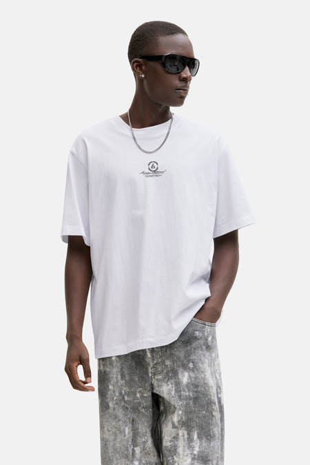 Wit T-shirt van CORE BY JACK & JONES, met een logo en tekstprint op de borst, gedragen met een zilveren ketting en grijze jeans.
