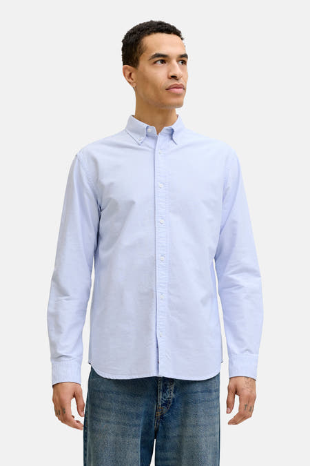 Chemise bleue à manches longues de PREMIUM BLUE by JACK & JONES, portée avec une veste marron et un jean ample.