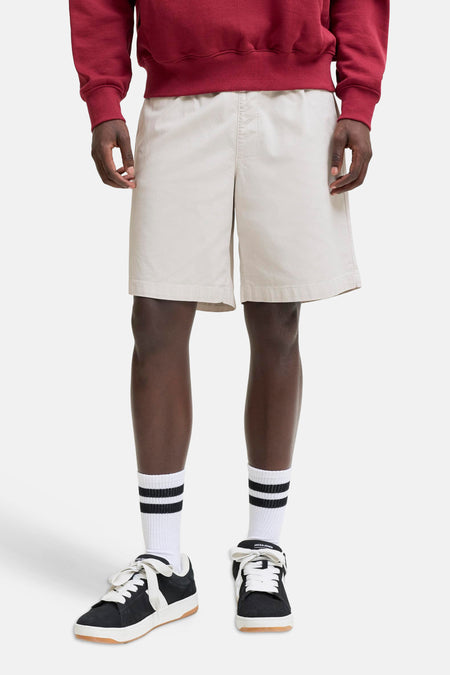 Beige short van JACK & JONES JEANS INTELLIGENCE, gedragen met een rood sweatshirt, gestreepte sokken en zwarte sneakers.
