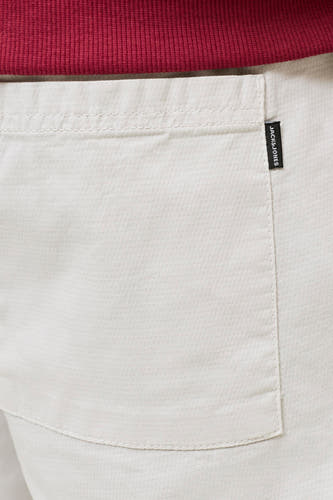 Beige short van JACK & JONES JEANS INTELLIGENCE met een geweven textuur, zichtbare zak met zwart label en een rood geribbelde stof erboven.