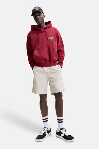 Beige short van JACK & JONES JEANS INTELLIGENCE, gedragen door een model met een rode hoodie, zwarte pet en sneakers.