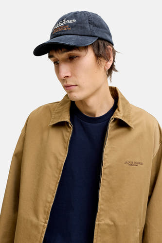 Blauwe denim pet van ACCESSORIES BY JACK & JONES met geborduurd logo, gedragen door model in beige jas en donkerblauw shirt, zijprofiel.