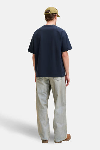 T-shirt bleu à manches courtes de ORIGINALS BY JACK & JONES, avec une coupe décontractée et porté avec une casquette verte et un jean clair.