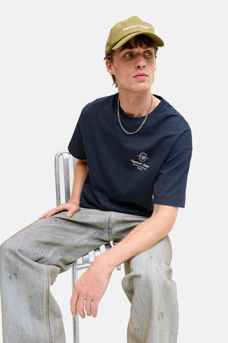 T-shirt bleu à manches courtes de ORIGINALS BY JACK & JONES, porté avec une chaîne argentée et un jean gris.