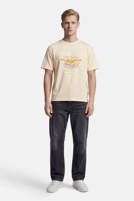 T-shirt écru à manches courtes de ORIGINALS BY JACK & JONES, avec imprimé huître et texte sur la poitrine, porté par un homme en jean foncé et baskets blanches.