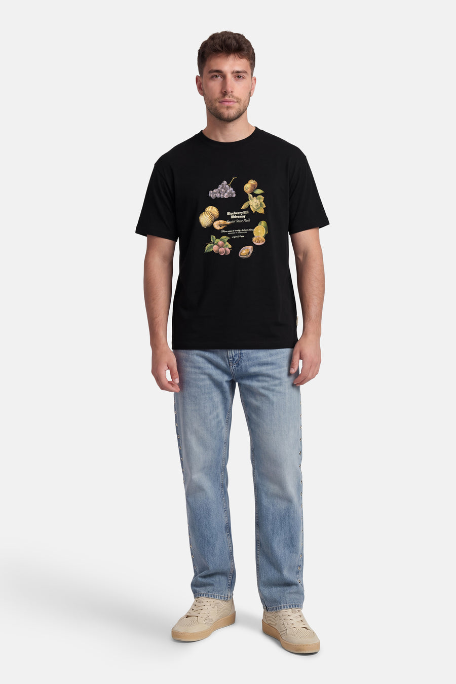 Zwart T-shirt van ORIGINALS BY JACK & JONES met kleurrijke fruit- en schelpdierprint, gedragen door een man met lichte jeans en beige sneakers.