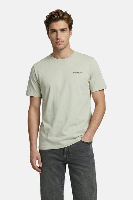 T-shirt à manches courtes vert de JJREBEL, avec le texte 'JJREBEL/23' sur la poitrine, porté par un homme avec un short en jean gris foncé.