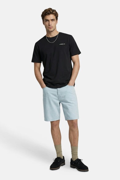 T-shirt noir à manches courtes de JJREBEL, avec col rond et texte blanc sur la poitrine, porté avec une chaîne argentée, un short en jean clair et des chaussettes beiges.