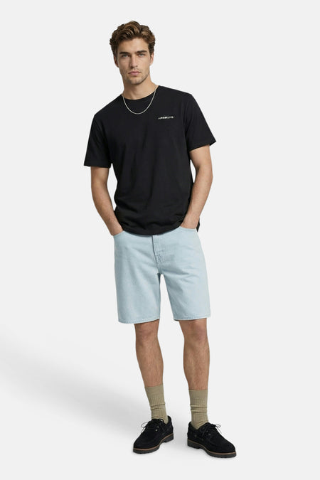 T-shirt noir à manches courtes de JJREBEL, avec col rond et texte blanc sur la poitrine, porté avec une chaîne argentée, un short en jean clair et des chaussettes beiges.