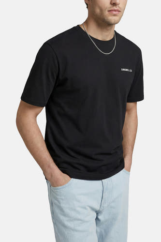 T-shirt noir de JJREBEL avec 'JJREBEL/23' blanc sur la poitrine, porté avec une chaîne argentée et un jean bleu clair.