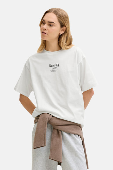 T-shirt blanc à manches courtes de JJXX, avec un imprimé, combiné avec un jogging gris et un pull marron.