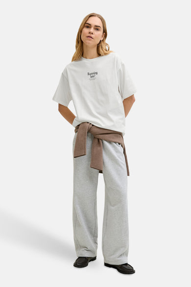 Wit T-shirt met korte mouwen van JJXX, met een opschrift, gecombineerd met grijze joggingbroek en bruine sweater.
