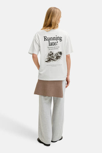 Wit T-shirt met korte mouwen van JJXX, met zwarte tekst en schoenillustratie op de achterkant, gedragen met een grijze broek.
