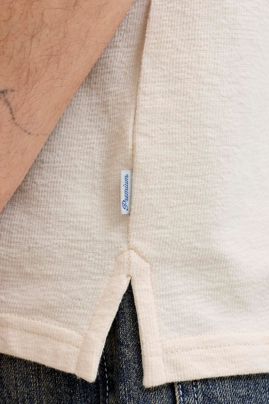 Beige korte mouwen T-shirt van PREMIUM by JACK & JONES, met ribstructuur en split aan onderkant, gedragen met donkerblauwe jeans, close-up zijaanzicht