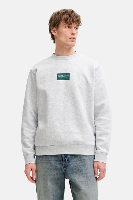 Grijze sweater van CORE BY JACK & JONES, met een logo op de borst, gecombineerd met een blauwe jeans.
