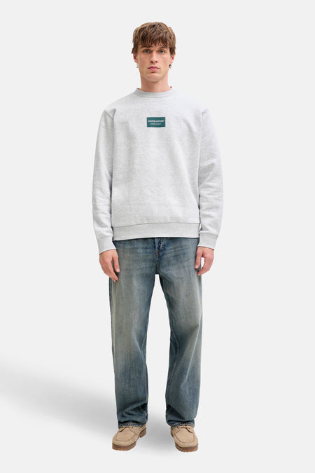 Grijze sweater van CORE BY JACK & JONES, met een vierkant groen logo op de borst en lange mouwen.