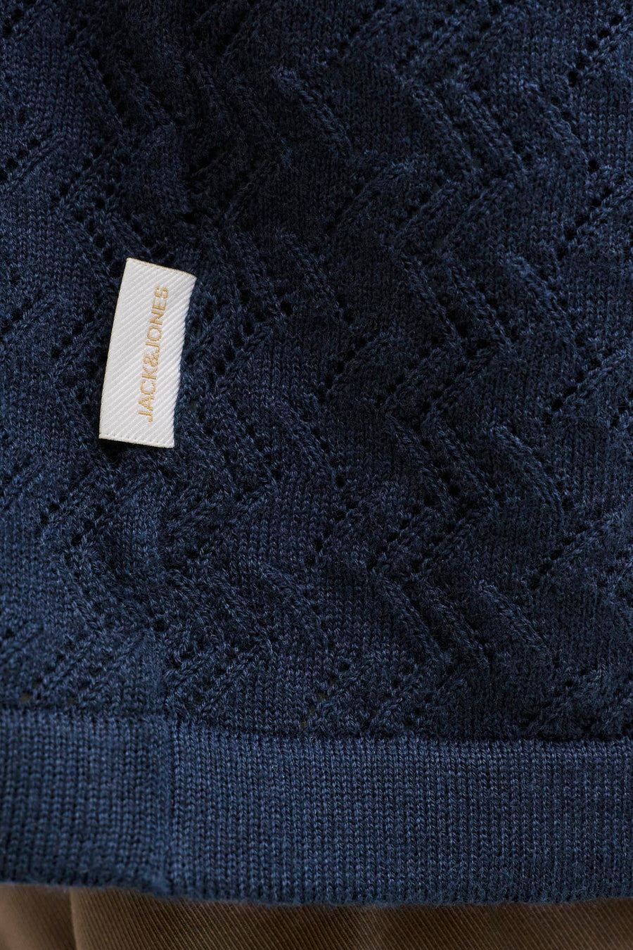 Polo en tricot bleu marine de Jack & Jones avec motif à carreaux ajouré, ourlet côtelé et étiquette blanche avec inscription dorée.