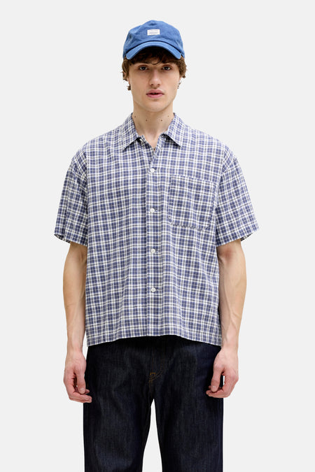 Blauw overhemd met korte mouwen van ORIGINALS BY JACK & JONES met blauw, wit en zwart ruitpatroon, knopen en borstzak, gedragen met blauwe pet en donkere spijkerbroek.