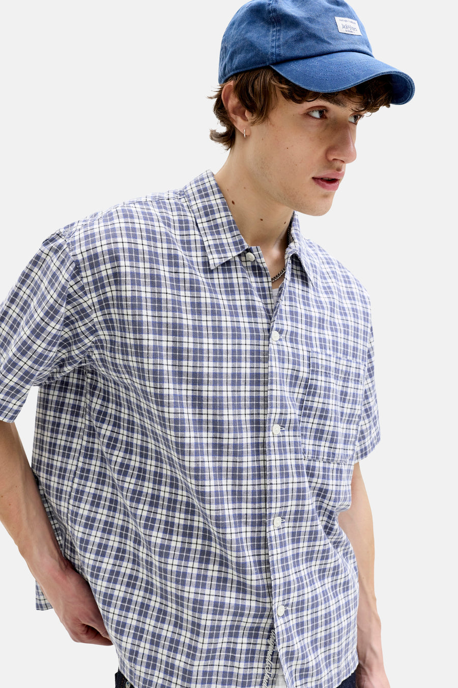 Blauw geruit overhemd met korte mouwen van ORIGINALS BY JACK & JONES, met witte knopen, gedragen door een model met blauwe pet en zilveren oorbel.