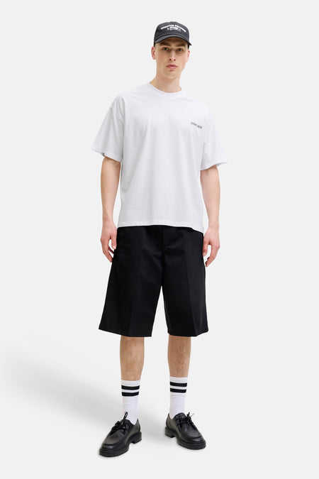 Wit T-shirt met korte mouwen van CORE BY JACK & JONES, met 'CORE 1980' print op de borst. Model draagt ook een zwarte pet, zwarte shorts en gestreepte sokken.